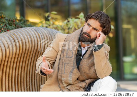 Sad unhappy frustrated Indian man sitting alone in city street, feeling bad, annoyed, grief, problem Sad unhappy frustrated Indian man sitting alone in city street, feeling bad, annoyed, grief, problem 128658987