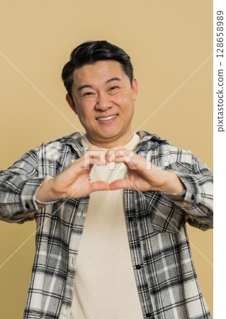 Happy Asian man makes heart gesture demonstrates love sign expresses good feelings and sympathy 128658989