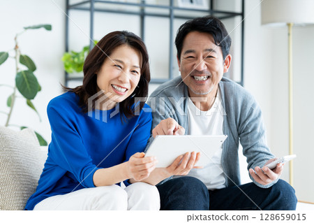 A middle-aged couple looking at a tablet in the living room A middle-aged couple looking at a tablet in the living room 128659015