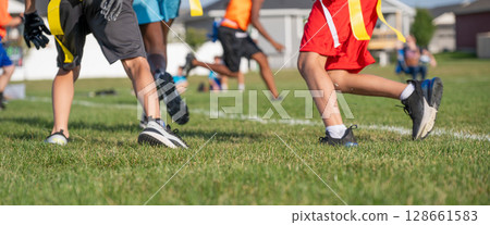 Youth athletes participate in flag football practice on a sunny day in a community park, showcasing teamwork and skill development 128661583