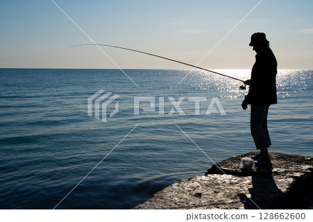 silhouette of a fisherman catches fish at sea 128662600