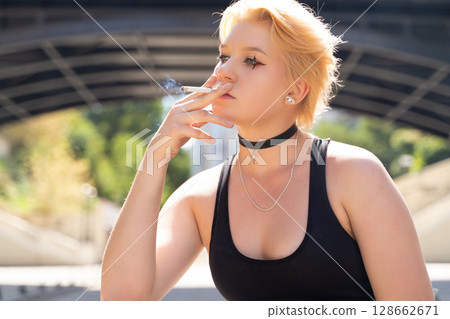 glamorous girl with short hair and makeup smoking a cigarette. glamorous girl with short hair and makeup smoking a cigarette. 128662671