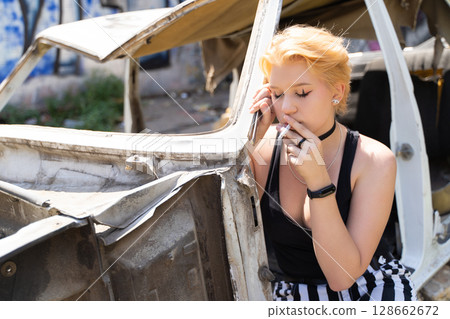 glamorous girl in pants and short hair and makeup posing near a broken old car. 128662672
