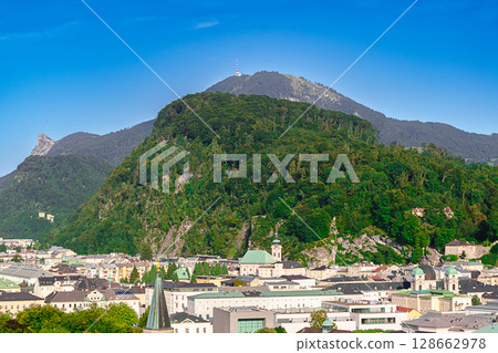 View over city of Salzburg in Austria, to Linzergasse with St. Sebastian Church at the foot of scenic hill Kapuzinerberg. In the back local mountain Gaisberg, and to the left the rocky peak Nockstein. View over city of Salzburg in Austria, to Linzergasse with St. Sebastian Church at the foot of scenic hill Kapuzinerberg. In the back local mountain Gaisberg, and to the left the rocky peak Nockstein. 128662978