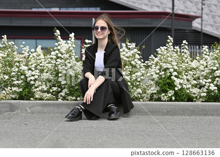 Woman in sunglasses smiling near white flowers on a sunny day outdoors. 128663136