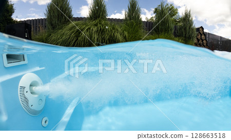 Underwater view of pool jet creating bubbles in a clean blue swimming pool with green plants and wooden fence in the backyard Underwater view of pool jet creating bubbles in a clean blue swimming pool with green plants and wooden fence in the backyard 128663518