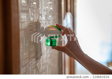 Woman hand plugs mosquito repellent into the socket before going to bed. Insect repellent diffuser. Woman hand plugs mosquito repellent into the socket before going to bed. Insect repellent diffuser. 128663816