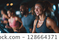Smiling woman running on treadmill in gym with energetic group in background 128664371