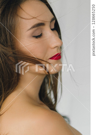 a beautiful sexy girl in a white men's shirt poses near a wall background 128665250