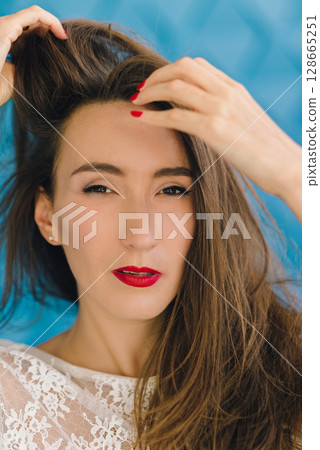 close-up portrait of a beautiful girl in a transparent white blouse posing against a background of a blue textured wall 128665251