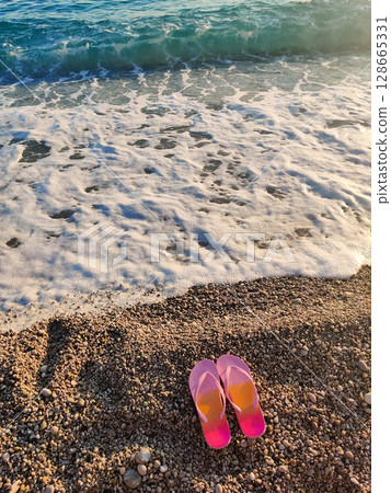 pink flip flops on sea beach in water waves 128665331