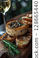Foie gras with a glass ampoule of white wine and rosemary jelly served on a rustic wooden board, accompanied by a sprig of fresh rosemary and a small side of toasted brioche 128665440