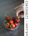 closeup hands are picking strawberries. Many fresh strawberries in a clear plastic glass lid on a wooden table background, fruit, food, decor, object, copy space 128665463
