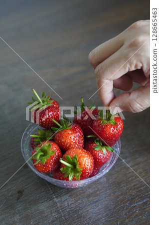 closeup hands are picking strawberries. Many fresh strawberries in a clear plastic glass lid on a wooden table background, fruit, food, decor, object, copy space closeup hands are picking strawberries. Many fresh strawberries in a clear plastic glass lid on a wooden table background, fruit, food, decor, object, copy space 128665463