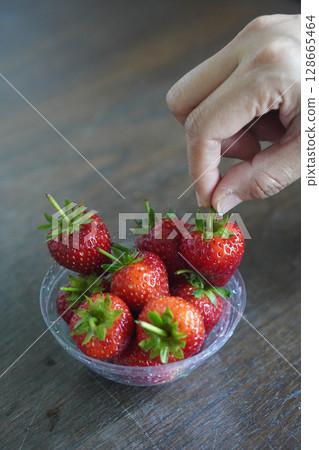 Hands are picking strawberries. Many fresh strawberries in a clear plastic glass lid on a wooden table background, fruit, food, decor, object, copy space Hands are picking strawberries. Many fresh strawberries in a clear plastic glass lid on a wooden table background, fruit, food, decor, object, copy space 128665464