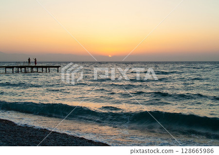 silhouette of people walking along the sea beach pier at sunset 128665986