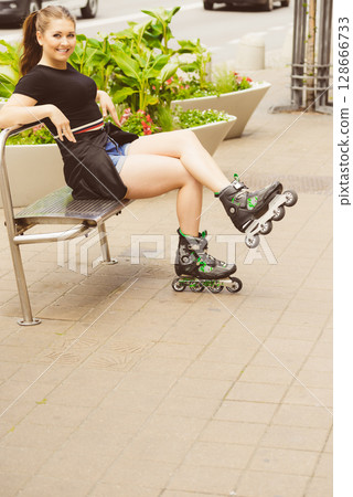 Young woman sitting wearing roller skates 128666733