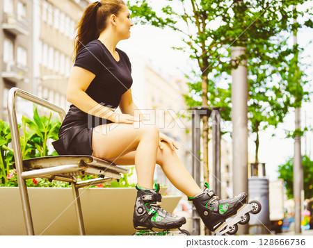 Young woman sitting wearing roller skates 128666736