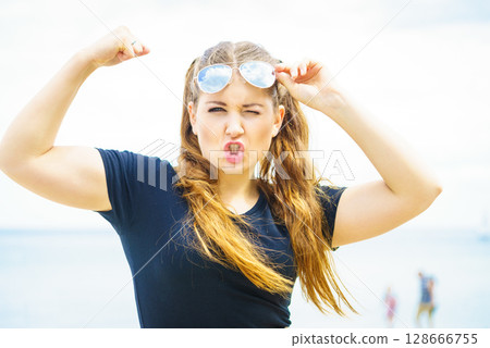 Woman in sunglasses showing muscles Woman in sunglasses showing muscles 128666755