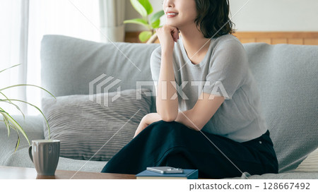 Smiling woman sitting on sofa in living room Smiling woman sitting on sofa in living room 128667492