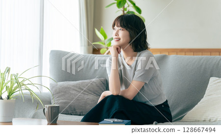 Smiling woman sitting on sofa in living room Smiling woman sitting on sofa in living room 128667494
