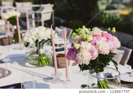 An elegant outdoor table setting adorned with beautiful bouquets of pink and white peonies 128667797