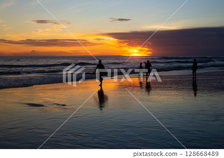 surfers catch a wave on the seashore at sunset 128668489