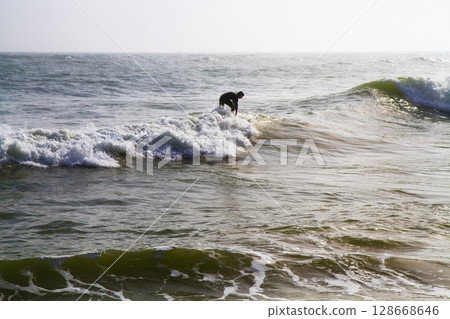 surfers with a board swim on stormy waves in the ocean 128668646