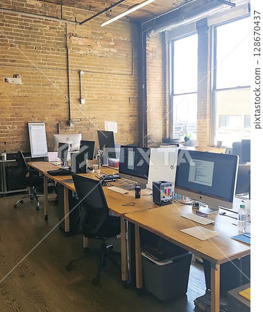 A row of computer desks with chairs and monitors 128670437