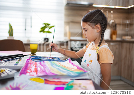 Cute girl painting a colorful masterpiece at home during the afternoon Cute girl painting a colorful masterpiece at home during the afternoon 128670518