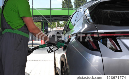 Petrol Station Worker holds a filling nozzle in his hands while refueling a car at a gas station 128671774