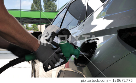 Assistant at petrol station hands in gloves inserting a fuel pistol into the gas tank of a car 128671775