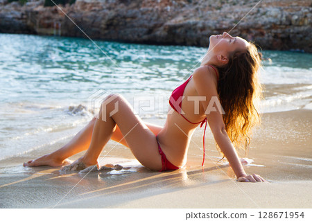 a beautiful girl in a red swimsuit is sunbathing on the beach a beautiful girl in a red swimsuit is sunbathing on the beach 128671954
