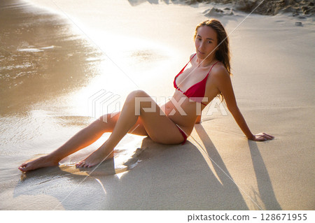 a beautiful girl in a red swimsuit is sunbathing on the beach a beautiful girl in a red swimsuit is sunbathing on the beach 128671955
