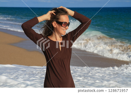 a beautiful girl in a brown dress is walking on the sandy beach and enjoying the sea view a beautiful girl in a brown dress is walking on the sandy beach and enjoying the sea view 128671957