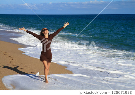 a beautiful girl in a brown dress is walking on the sandy beach and enjoying the sea view 128671958