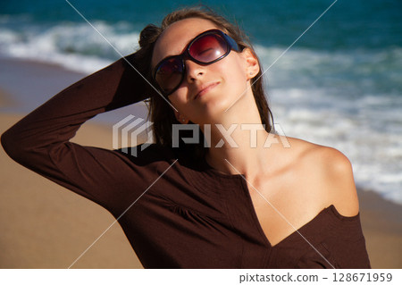 a beautiful girl in a brown dress is walking on the sandy beach and enjoying the sea view 128671959