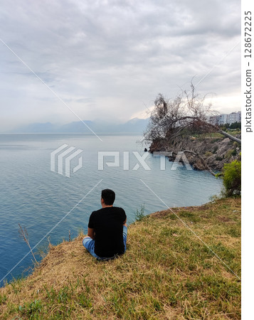 a guy sits on the seashore looking into the distance a guy sits on the seashore looking into the distance 128672225