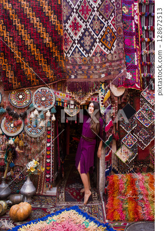 a beautiful girl in dress in a traditional turkish interior with many carpets on the wall 128672513