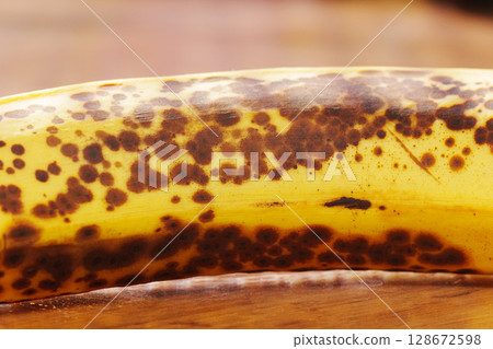 A ripe banana with dark brown spots lies on a wooden surface in a kitchen 128672598