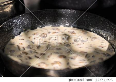 A pot of creamy mushroom sauce simmers on the stove. The sunlight casts shadows on the mixture as the cook A pot of creamy mushroom sauce simmers on the stove. The sunlight casts shadows on the mixture as the cook 128672629