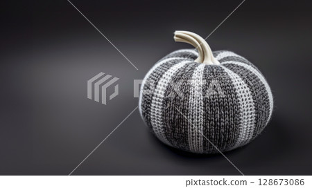 Knitted black and white pumpkin on dark background, highlighting sustainable Halloween decor. Perfect for DIY enthusiasts, showcasing handmade gifts and eco-friendly holiday decorations. Copy space 128673086