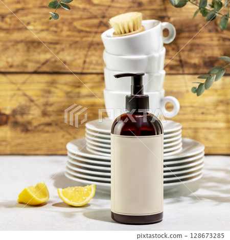 Mockup of organic dish detergent. Eco friendly natural cleaning dishes. Bottle with dish detergent with clean plates and cups on wooden background with sprig of eucalyptus. Front view 128673285