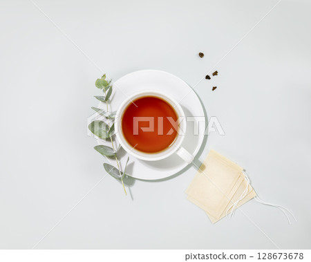 Cup of tea. Eco friendly still life with cup of tea, eucalyptus sprig and paper tea bags on blue background. Concept of organic tea and healthy natural drink. Flat lay Cup of tea. Eco friendly still life with cup of tea, eucalyptus sprig and paper tea bags on blue background. Concept of organic tea and healthy natural drink. Flat lay 128673678