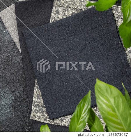 Folded black napkins on black background with green leaves. Eco friendly Mock up for display or montage of dishes, food or washing detergent. Showcase for presentation. Flat lay 128673687