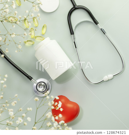 Mockup of vitamins and supplements for healthy heart. White bottle with gel capsules, stethoscope and heart shape hand exercise ball on blue background. Flat lay 128674321