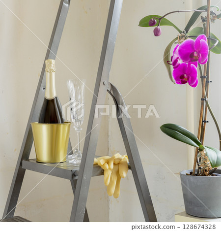 Romantic still life with bottle of champagne and glasses on stepladder against an unpainted wall with potted orchid. Moving of young family. Mortgage concept. Real estate, moving home or renovation Romantic still life with bottle of champagne and glasses on stepladder against an unpainted wall with potted orchid. Moving of young family. Mortgage concept. Real estate, moving home or renovation 128674328