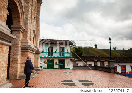 Senior woman traveling concept. Buildings around the Jose Maria Cordova Park and Our Lady of the Immaculate Conception Church in the beautiful colonial town of Concepcion in Antioquia, Colombia. 128674347