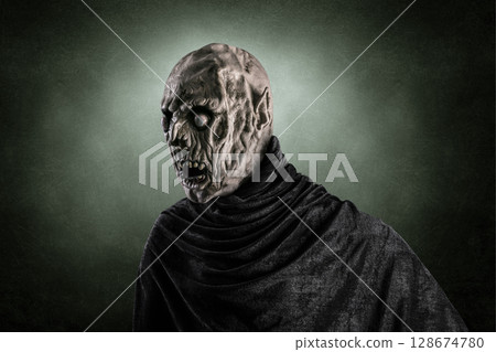 Portrait of a zombie with hooded cape over dark green misty background 128674780