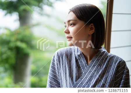 A young woman in a yukata sitting by the window at a ryokan 128675155